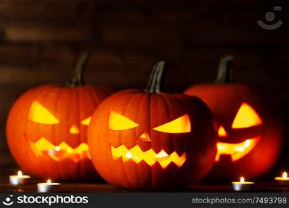 Three Halloween pumpkins head jack o lantern and candles on wooden table background. Halloween pumpkins and candles