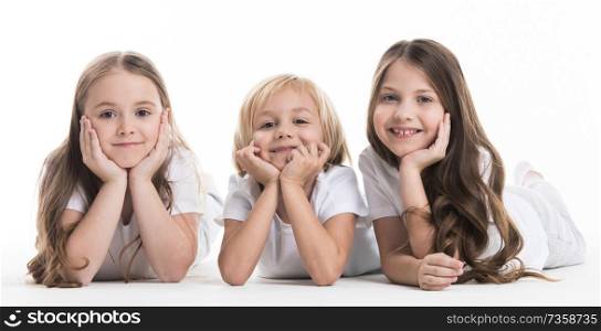 Three happy children laying on floor resting head on hands isolated on white background. Three happy children laying on floor