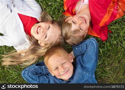 Three happy children lying on the grass