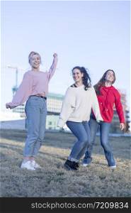 Three happy excited young adult women in casual dresses celebrate victory and jumping
