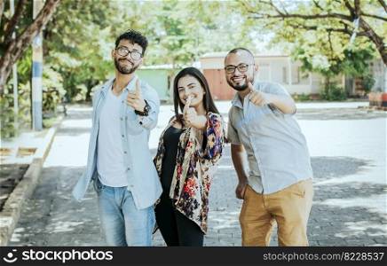 Three happy friends giving thumbs up on the street. Three smiling teenagers giving thumbs up on the street. Team concept of smiling friends giving thumbs up on the street