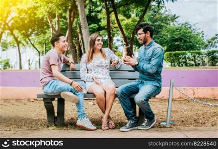 Three happy friends talking in a park. Three teenage friends talking sitting on a park bench, Group of three friends talking sitting in a park. Concept of people talking in the park