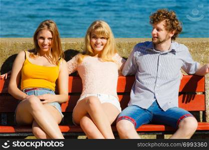 Three happy smiling young people friends outdoor. Attractive women and handsome man sitting on bench. Summer vacation.. Three happy young people friends outdoor.
