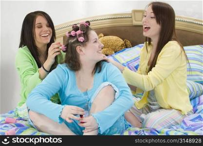 Three happy teen girls at slumber party doing hair and fingernails.