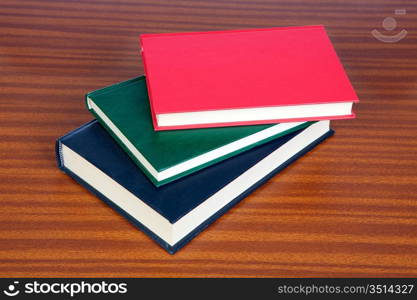 Three hardcover books on a wooden surface