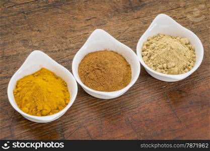 three healthy spices (turmeric, ginger and cinnamon) in white bowls on a grunge wood