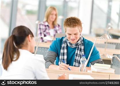 Three high school students in classroom studying with books and laptop