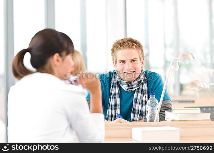 Three high school students in classroom studying with books and laptop