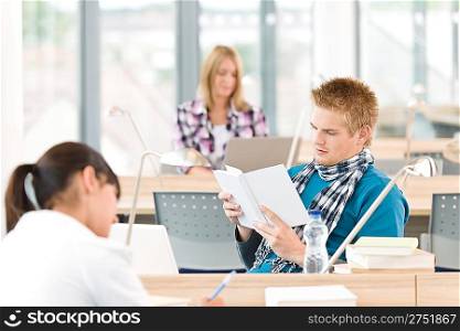 Three high school students in classroom studying with books and laptop