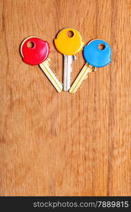 Three house keys with colorful plastic coats caps on wooden table background. Copy space for text