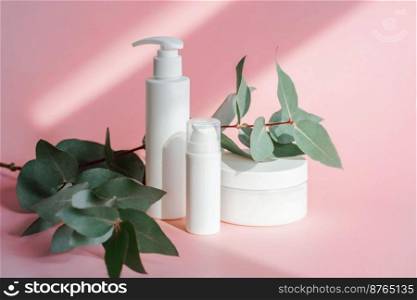 Three jars of cosmetics stand on a pink background, flooded with sunlight. This is a cream, serum and foam for washing. Nearby lies greenery. Front view.. Three jars of cosmetics stand on a pink background.