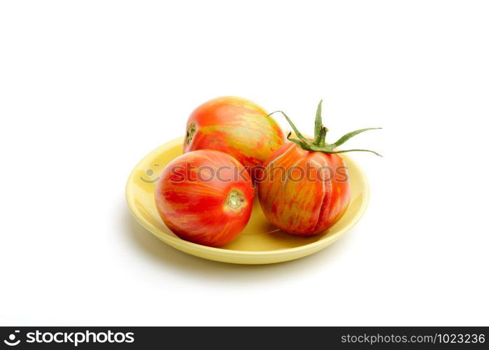 Three juicy red zebra tomatoes in a little yellow porcelain plate, isolated on white background