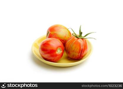 Three juicy red zebra tomatoes in a little yellow porcelain plate, isolated on white background