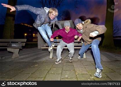 Three juveniles leaping off a park bench, ready for a fight