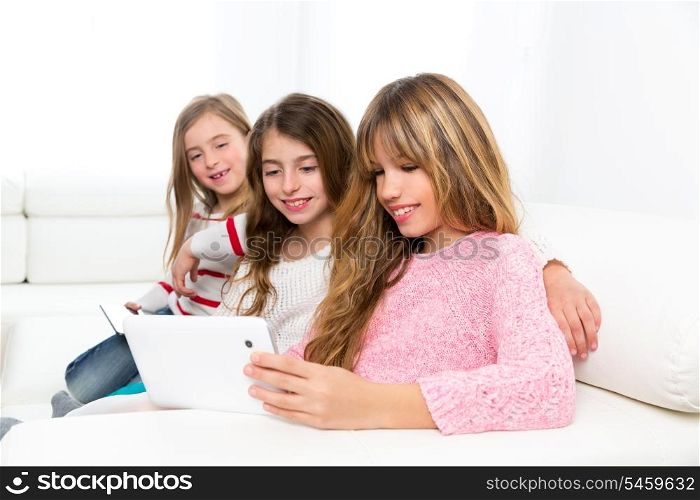 three kid sister friends girls group playing together with tablet pc on white sofa