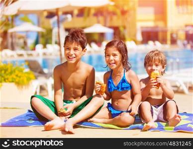 Three kids sitting down and eating croissant near pool, picnic outdoors, beach resort, summer vacation, happy childhood concept