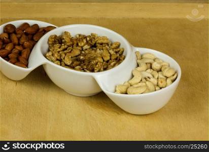 Three kinds of fresh nuts ,Indian almonds,(Macadamia) walnuts, hazelnuts in a white bowl. Healthy eating . Close, horizontal view.