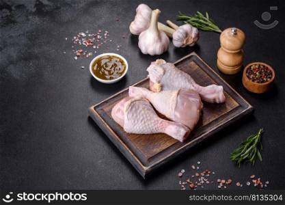 Three legs of raw chicken with spices and herbs on a wooden cutting board against a dark concrete background. Cooking at home. Three legs of raw chicken with spices and herbs on a wooden cutting board