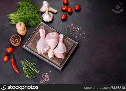Three legs of raw chicken with spices and herbs on a wooden cutting board against a dark concrete background. Cooking at home. Three legs of raw chicken with spices and herbs on a wooden cutting board