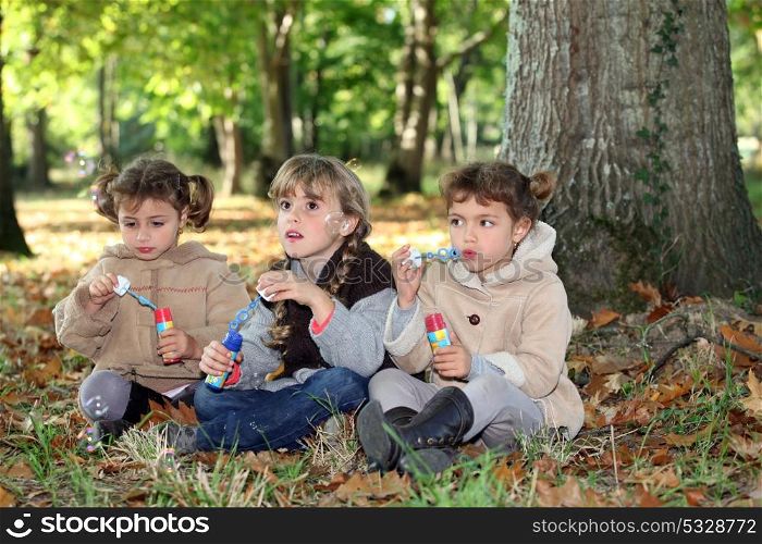 three little girls playing with soap bubble solutions in the forest