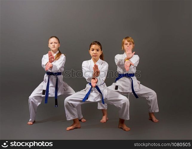 three little karate girls in a white kimono and blue belts perform a beautiful team kata on a dark background. three karate girls