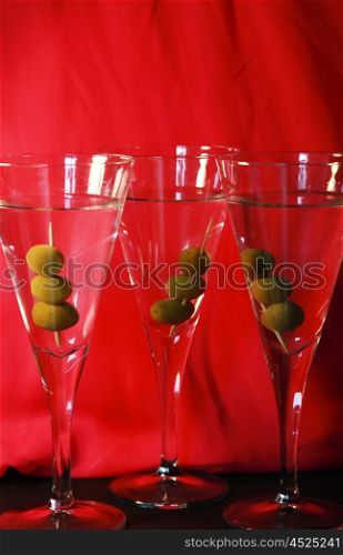 Three martini cocktails with olives against a bright red backdrop