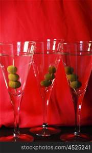 Three martini cocktails with olives against a bright red backdrop