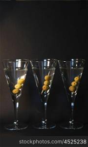 Three martini cocktails with olives against a dark backdrop