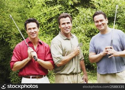 Three mature men holding golf clubs and smiling