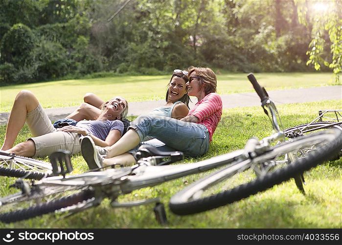 Three mature woman relaxing on grass after bicycle ride