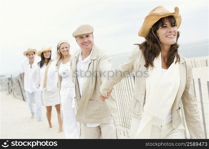 Three mature women and two mature men holding each other&acute;s hands on the beach