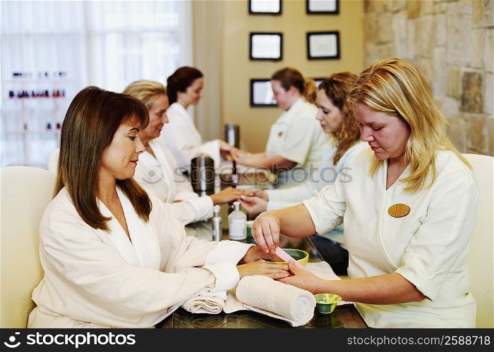 Three mature women getting manicure by beauticians