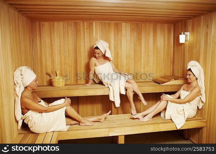 Three mature women wearing towels sitting in a sauna