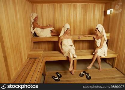 Three mature women wearing towels sitting in a sauna