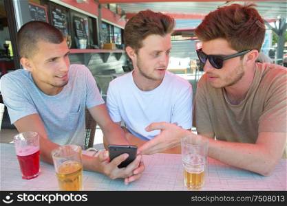 Three men in bar looking at cellphone