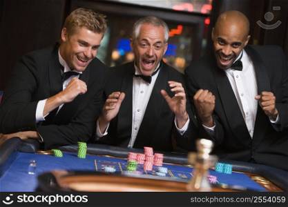 Three men in casino playing roulette smiling (selective focus)