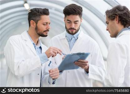 three men in labcoats looking at clipboard