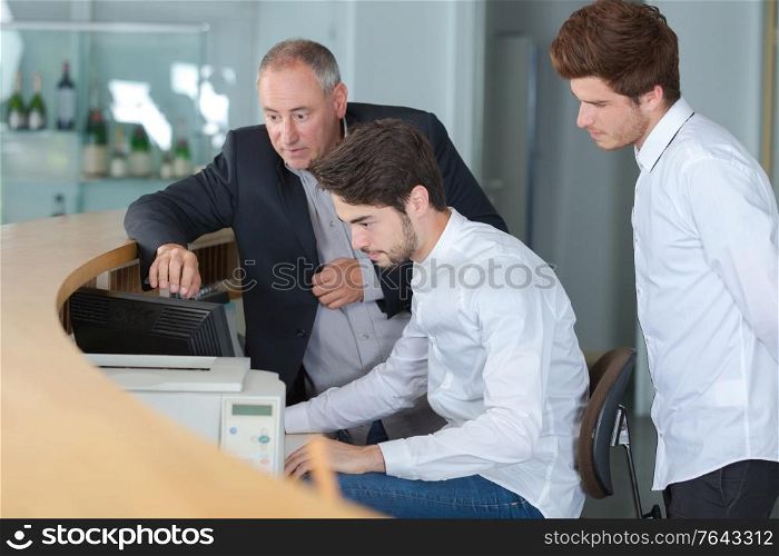 Three men looking at computer behind reception desk