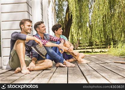 Three men sitting on wooden decking, looking away
