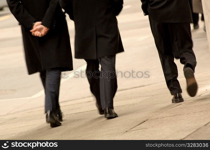 Three men walking downtown wearing black coats.