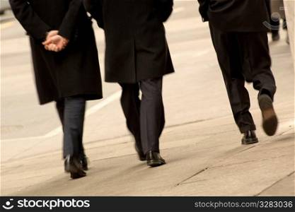 Three men walking downtown wearing black coats.