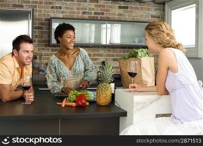 Three mid-adult friends having glass of wine in kitchen