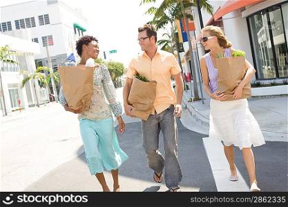 Three mid-adult friends on street holding groceries