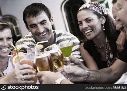 Three mid adult men and two mid adult women toasting their drinks
