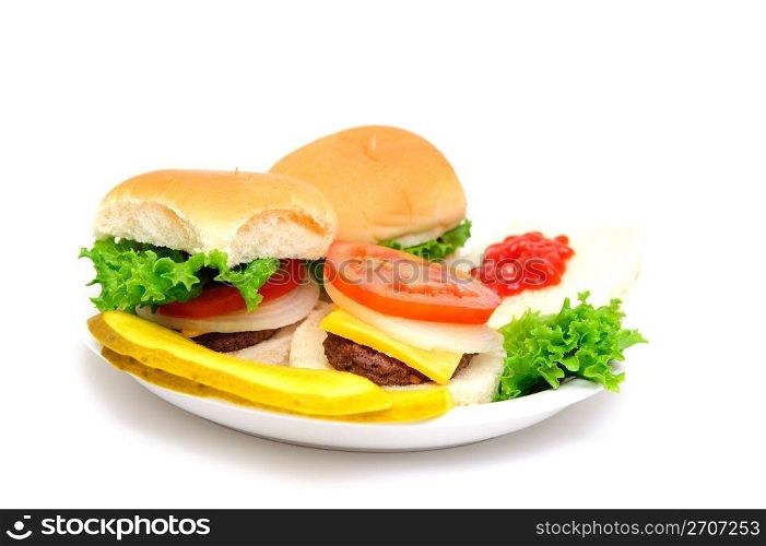 Three mini-burgers topped with cheddar cheese, white onion, tomato and lettuce on a white plate with sliced dill pickels on the side isolate on a white background. Mini-hamburgers