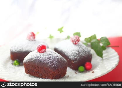 Three miniature chocolate cakes with powdered sugar, fresh raspberries and small Christmas ornaments