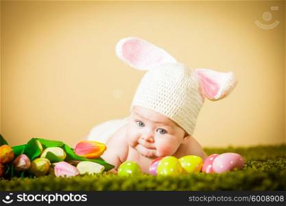 Three months baby lying on his stomach as a Easter bunny on the grass with eggs. Baby Easter bunny