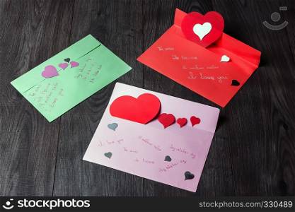 Three multi-colored envelope with a declaration of love written in different languages and paper hearts.. Declarations of love for Valentine?s Day