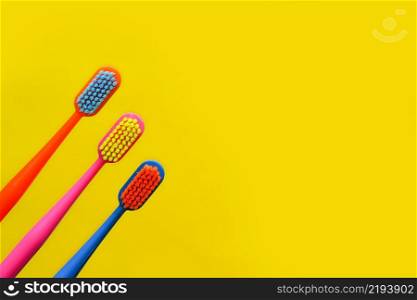 three multi-colored toothbrushes and a figurine of a tooth on a yellow background. dentistry advertising concept. copy space.