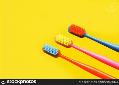 three multi-colored toothbrushes and a figurine of a tooth on a yellow background. dentistry advertising concept. copy space.